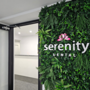 Serenity Dental A greenery wall (various lush green fake plants) with the Serenity Dental logo in the middle. Displayed inside an office.